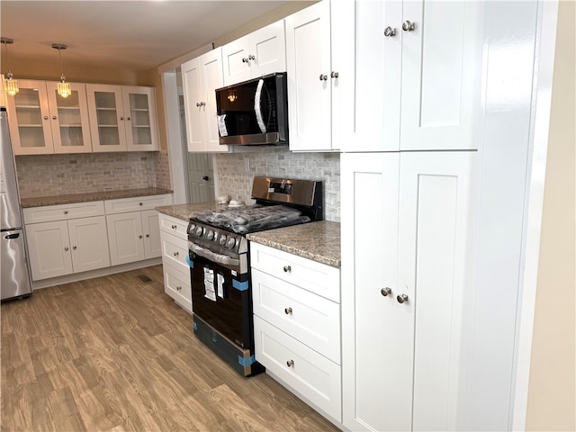 kitchen featuring appliances with stainless steel finishes, pendant lighting, tasteful backsplash, white cabinets, and light hardwood / wood-style flooring