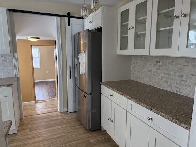 kitchen with stainless steel refrigerator, tasteful backsplash, white cabinets, dark stone counters, and a barn door