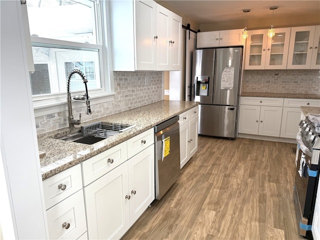 kitchen featuring appliances with stainless steel finishes, pendant lighting, sink, white cabinets, and a barn door