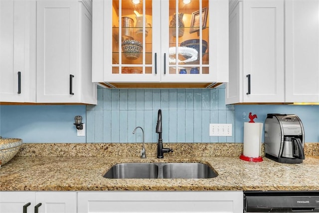 kitchen with dishwashing machine, light stone counters, a sink, glass insert cabinets, and white cabinetry