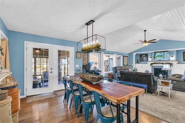 dining room with a ceiling fan, wood finished floors, french doors, a fireplace, and vaulted ceiling