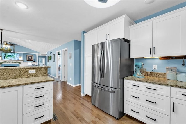 kitchen with lofted ceiling, light wood-style flooring, light stone countertops, and freestanding refrigerator