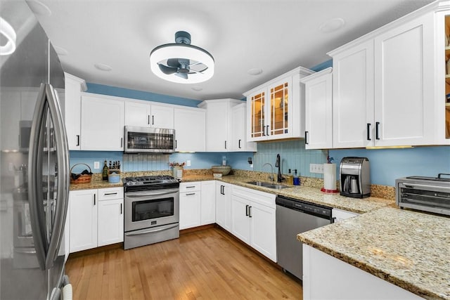 kitchen featuring a sink, glass insert cabinets, appliances with stainless steel finishes, white cabinetry, and light wood-type flooring