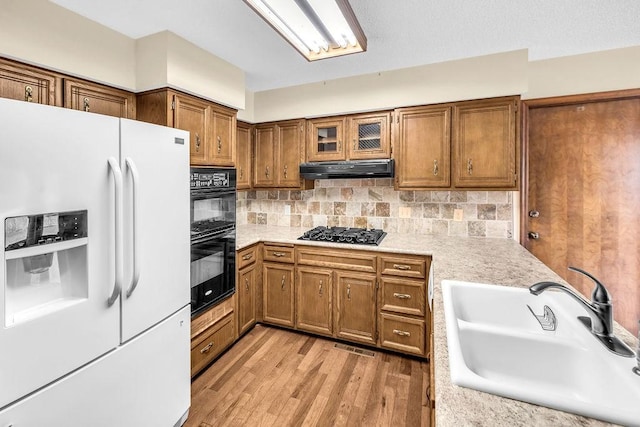4554 Nicklaus Ct, Decatur, IL 62526 - kitchen with black appliances, under cabinet range hood, brown cabinets, a sink, and light countertops
