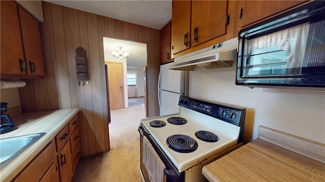 kitchen with sink, wooden walls, white fridge, a notable chandelier, and range with electric cooktop