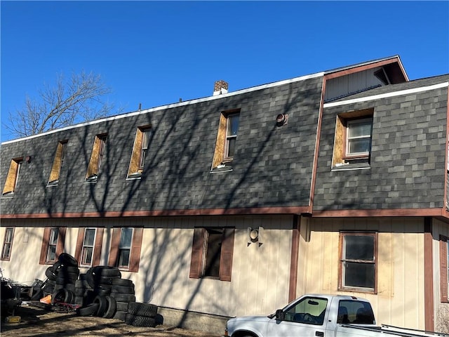 view of side of property with roof with shingles, a chimney, and mansard roof