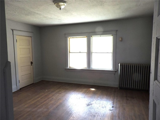 empty room featuring a textured ceiling, radiator heating unit, wood finished floors, and baseboards