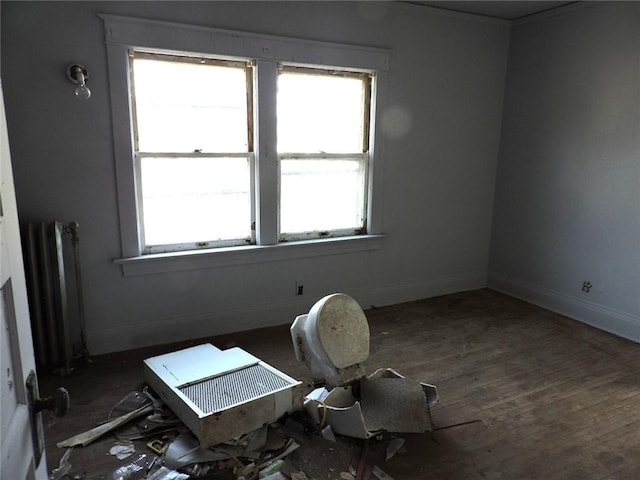 empty room with baseboards, wood finished floors, and radiator