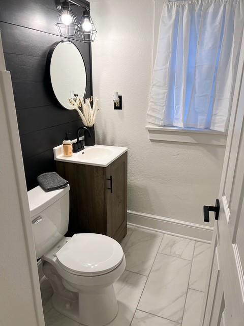 half bath with baseboards, marble finish floor, toilet, and vanity