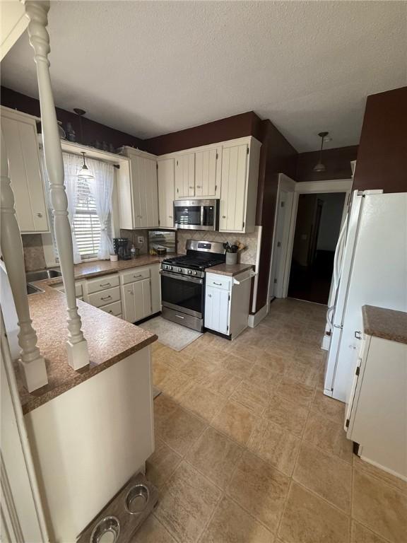 kitchen with a textured ceiling, appliances with stainless steel finishes, backsplash, and white cabinetry