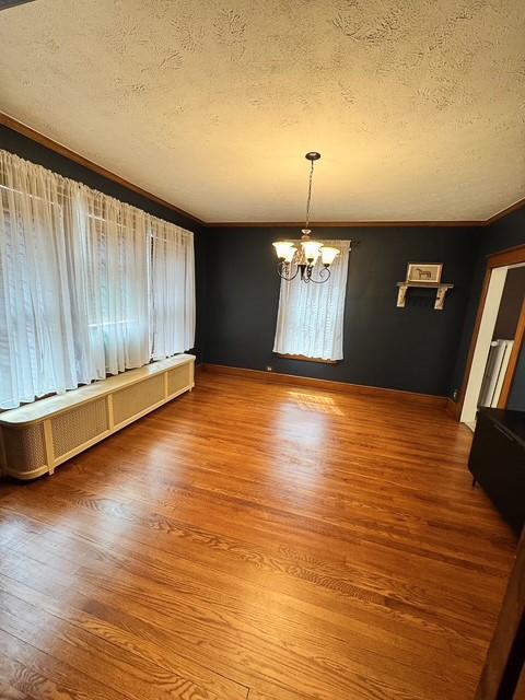unfurnished dining area with wood finished floors, a textured ceiling, a baseboard heating unit, and a notable chandelier