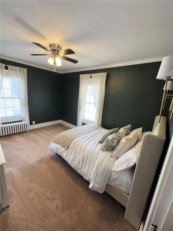 bedroom with a ceiling fan, baseboards, radiator, ornamental molding, and carpet flooring