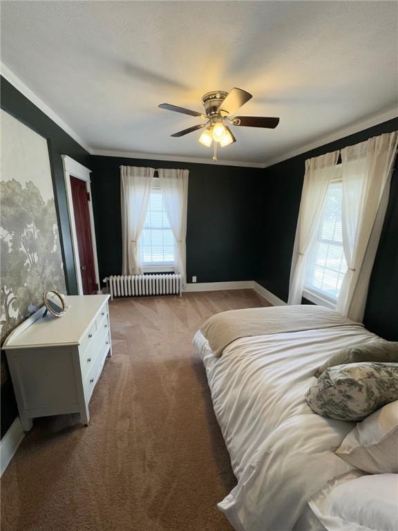 carpeted bedroom featuring a ceiling fan, baseboards, ornamental molding, and radiator