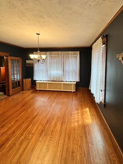 spare room featuring a notable chandelier, a textured ceiling, baseboards, wood finished floors, and ornamental molding