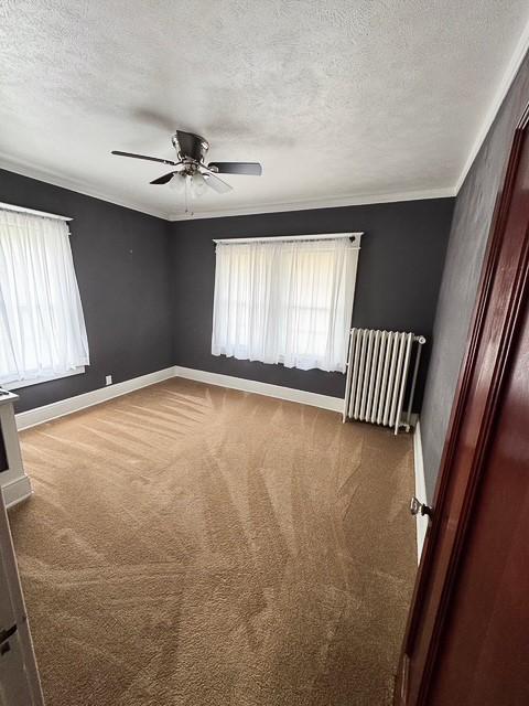 carpeted empty room featuring crown molding, a textured ceiling, radiator heating unit, a ceiling fan, and baseboards