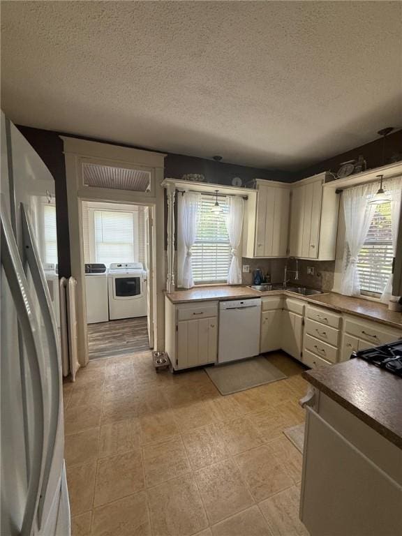 kitchen featuring white appliances, a textured ceiling, plenty of natural light, and washer and clothes dryer