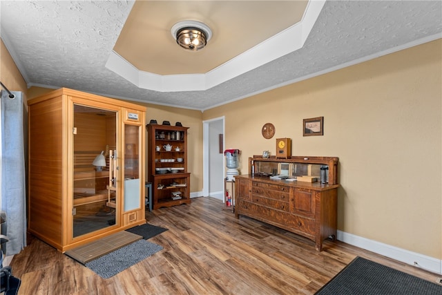 living area with wood-type flooring, a textured ceiling, a tray ceiling, and crown molding