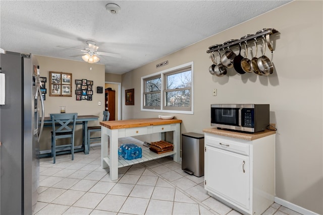 kitchen with ceiling fan, butcher block countertops, a textured ceiling, white cabinets, and appliances with stainless steel finishes