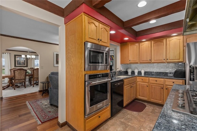 kitchen featuring a sink, an inviting chandelier, tasteful backsplash, arched walkways, and appliances with stainless steel finishes