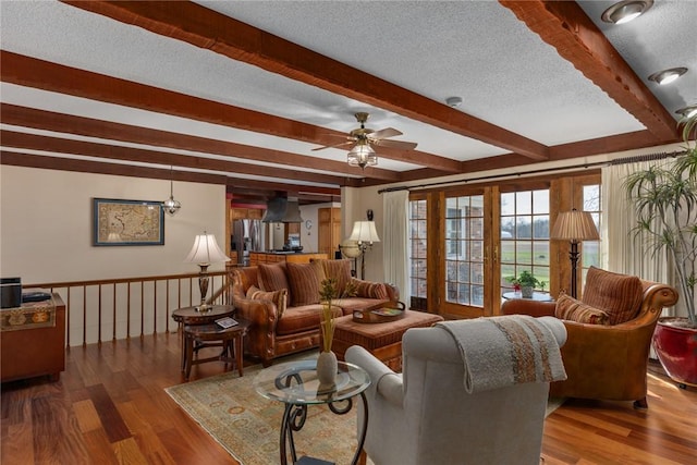 living room featuring a textured ceiling, wood finished floors, a ceiling fan, and beamed ceiling