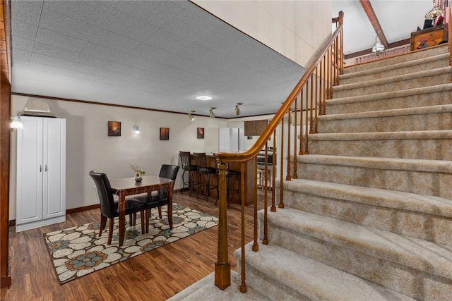 dining space with baseboards, wood finished floors, stairs, and crown molding