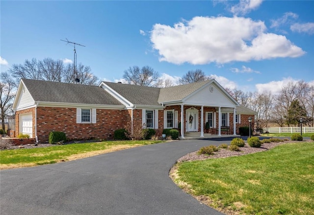 neoclassical / greek revival house with a front yard, fence, a porch, brick siding, and a garage