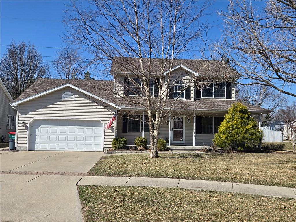 traditional-style house with a front lawn, a garage, driveway, and roof with shingles