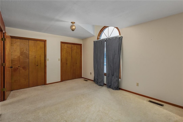 unfurnished bedroom featuring two closets and light colored carpet