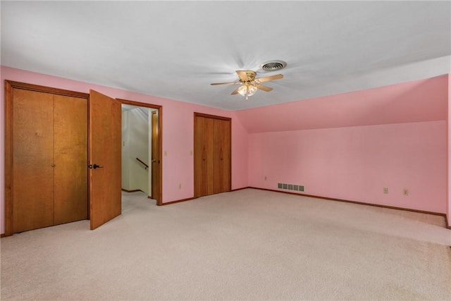 unfurnished bedroom with lofted ceiling, multiple closets, light carpet, and ceiling fan