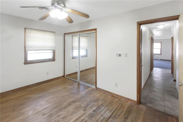 unfurnished bedroom with ceiling fan, baseboards, baseboard heating, wood finished floors, and a closet