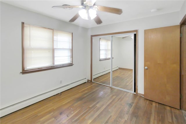 unfurnished bedroom with a closet, a baseboard heating unit, ceiling fan, and wood finished floors