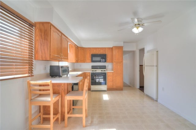 kitchen featuring black microwave, light countertops, range with gas stovetop, a peninsula, and freestanding refrigerator