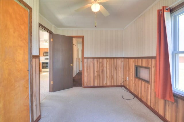 unfurnished room with wallpapered walls, ceiling fan, a wainscoted wall, ornamental molding, and carpet floors