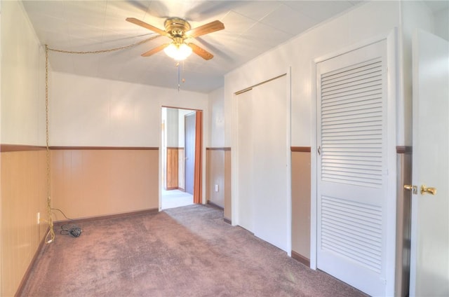 carpeted spare room featuring a wainscoted wall and ceiling fan