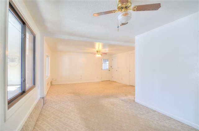 empty room featuring light colored carpet, a textured ceiling, baseboards, and a ceiling fan