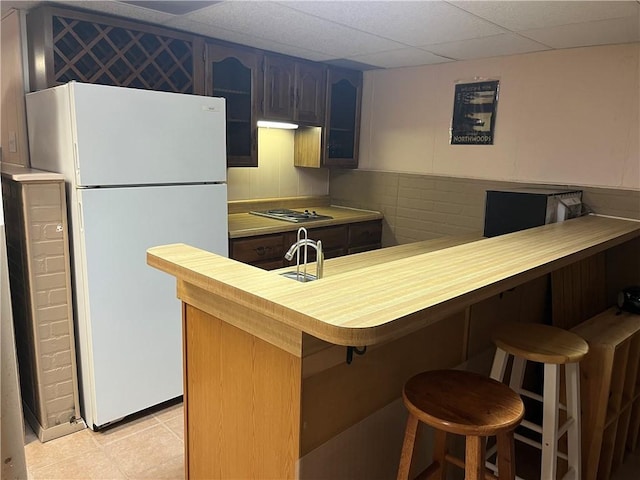 kitchen with a kitchen breakfast bar, kitchen peninsula, a paneled ceiling, cooktop, and white fridge