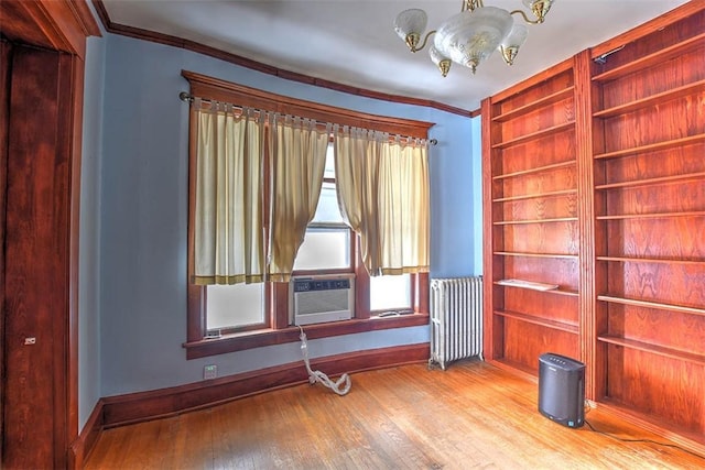 empty room featuring radiator heating unit, wood-type flooring, cooling unit, built in features, and ornamental molding