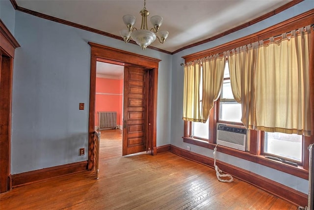 spare room featuring a notable chandelier, a healthy amount of sunlight, hardwood / wood-style flooring, and radiator heating unit