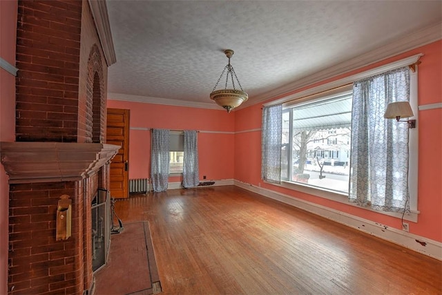 unfurnished living room featuring a brick fireplace, hardwood / wood-style floors, radiator, ornamental molding, and a textured ceiling