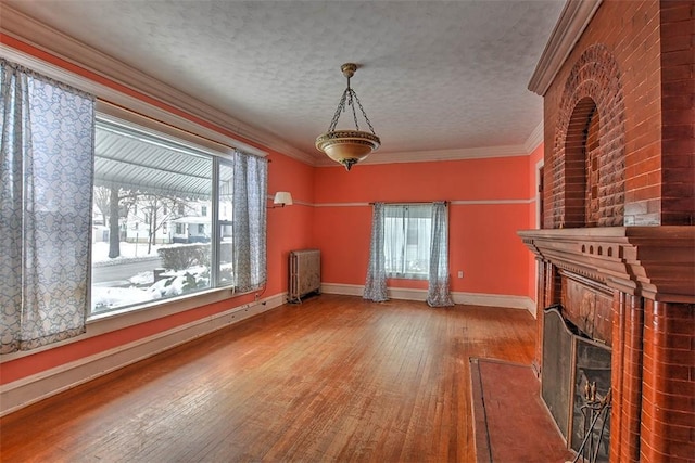 unfurnished living room featuring a brick fireplace, a textured ceiling, radiator, and ornamental molding