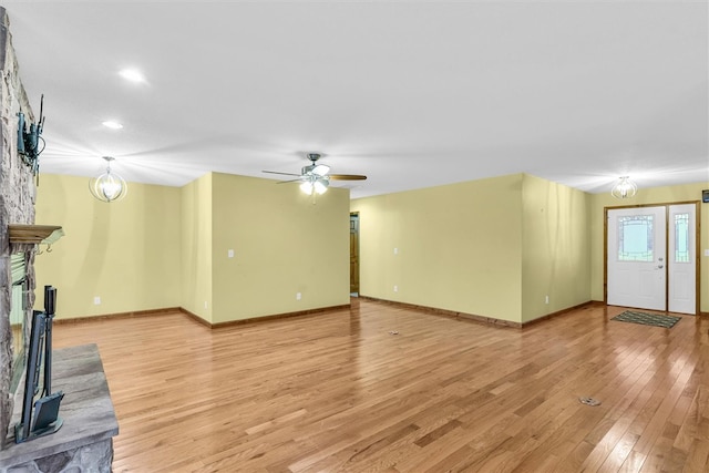 unfurnished living room with ceiling fan with notable chandelier, light wood-type flooring, and a fireplace