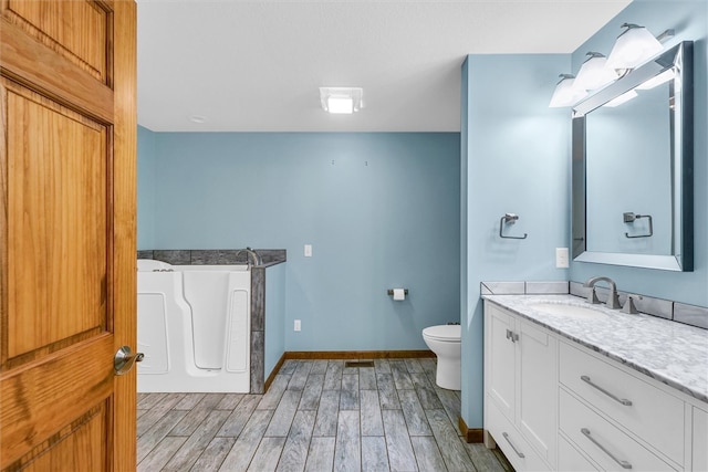 bathroom with a bathtub, vanity, wood-type flooring, and toilet