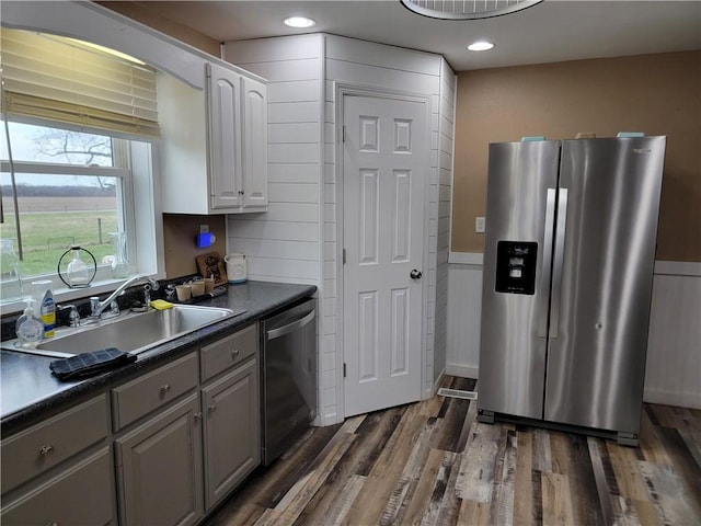 kitchen featuring stainless steel appliances, dark countertops, a sink, dark wood-style floors, and gray cabinets