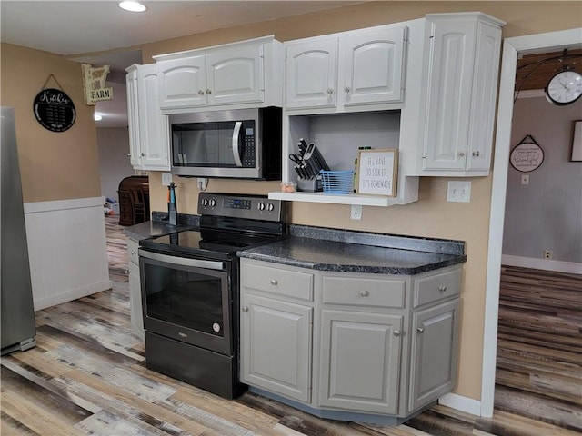 kitchen with light wood-style flooring, baseboards, dark countertops, white cabinets, and appliances with stainless steel finishes