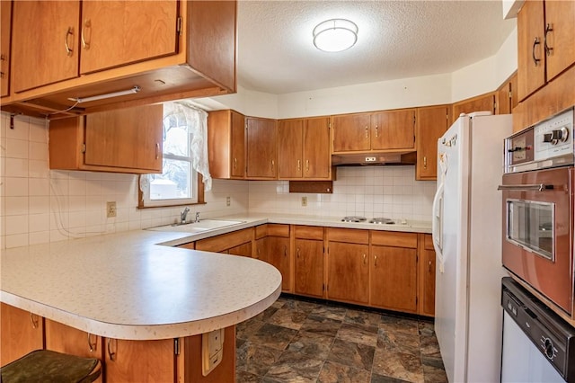 kitchen with under cabinet range hood, a peninsula, white appliances, a sink, and brown cabinets