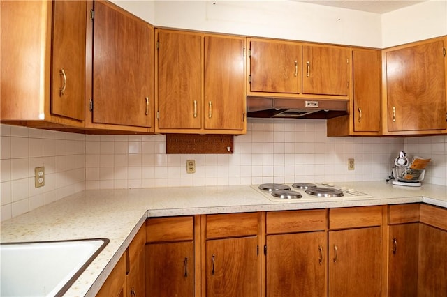 kitchen featuring white electric stovetop, light countertops, a sink, and under cabinet range hood