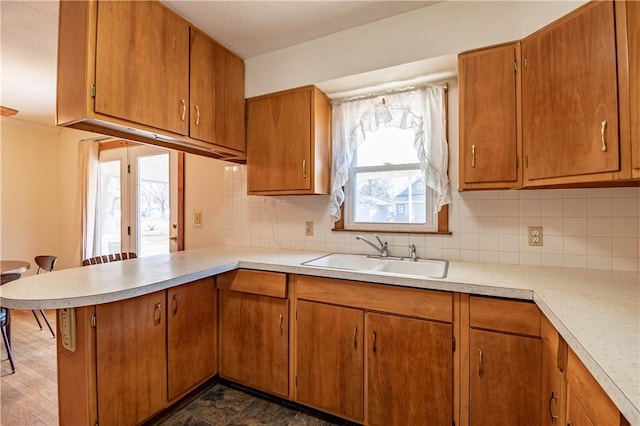 kitchen featuring decorative backsplash, brown cabinets, a peninsula, light countertops, and a sink