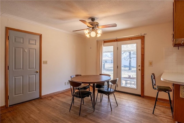 dining space featuring a textured ceiling, ornamental molding, light wood-type flooring, and baseboards