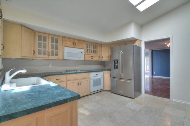 kitchen with dark countertops, tasteful backsplash, a sink, glass insert cabinets, and white appliances