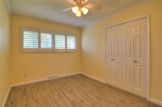unfurnished bedroom with baseboards, visible vents, ornamental molding, and wood finished floors